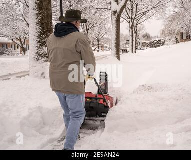 Berks County, Pennsylvania-February 2, 2021:  Senior man using a snow blower to clear his sidewalk and driveway after snowstorm Stock Photo