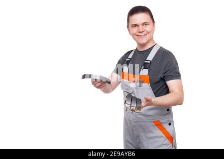 male employee in gray uniform of car mechanic worker with spanner wrench in pocket holds brake shoes inhands looks into camera and smiles isolated on Stock Photo