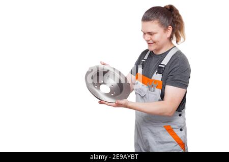 brunette male engineer workman in gray uniform of working car mechanic with a spanner wrench in pocket holds brake disc in hands looks at car brakes s Stock Photo
