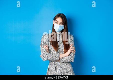 Covid-19, pandemic lifestyle concept. Pensive girl in medical mask look at upper left corner logo, thinking ways of protecting health from coronavirus Stock Photo