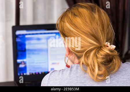 Selective focus shot of a blonde woman searching something on her laptop - work from home concept Stock Photo
