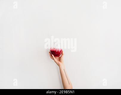 Human hand holding glass with purple beet pomegranate fresh homemade smoothie with glass straw, white background, copy space. Detox, dieting, weight loss, healthy lifestyle concept Stock Photo