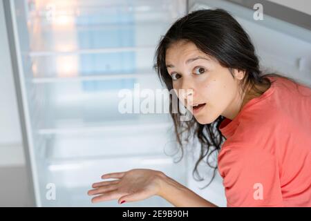 The girl is surprised at the empty refrigerator. Lack of food. Food delivery. Stock Photo