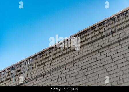 Roof of old building covered with sharp icicles. Large icicles hanging from the roof of an old brick building. Ice stalactite. Poor roof insulation Stock Photo