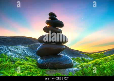 Stacked Pebbles art on mossy rocks welcomes beautiful new day Stock Photo