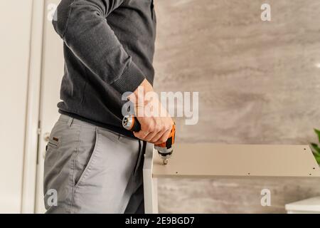 Midsection of man Putting Together Self Assembly Furniture at Home holding electric screwdriver using to join plywood parts - half length front view D Stock Photo