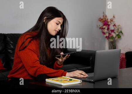 Portrait of a pretty woman working from home on her laptop sitting in living room, young girl studying from home, video conference with friend. Stock Photo