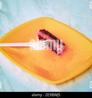 Grilled sausage on a white fork on a yellow plastic plate Stock Photo