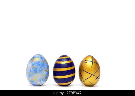 Three easter eggs trendy colored classic blue, white and golden decorated on white table. Happy Easter card with copy space for text. Minimal style Stock Photo