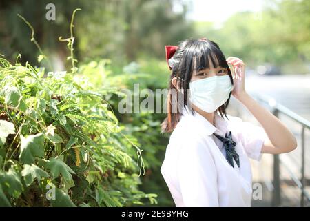 Asian school girl with mask in urban city with tree background Stock Photo