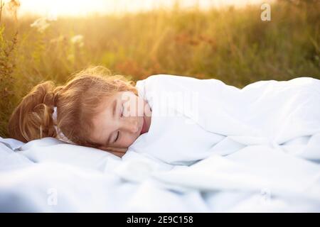 The girl sleeps on white bed linen in nature in the grass, in the fresh air. Eco-friendly lifestyle, healthy sleep, the benefits of ventilation, harde Stock Photo