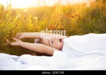 Girl sleeps on bed in grass, Sweet stretches and yawns sleepily, good morning in fresh air. Eco-friendly, healthy sleep, benefits of ventilation, hard Stock Photo