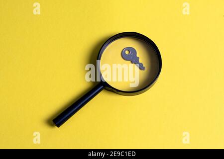 Magnifying glass with key on yellow background. Concept image of finding solution Stock Photo