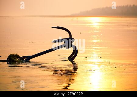 Fishing boat rusty traditional anchor on a beach by the sea.Golden sunlight on sandy beach. Stock Photo