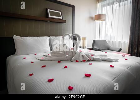 Romantic cozy boutique hotel room getaway with gorgeous swan towels red rose petals spread on bed waiting valentine guests on honeymoon anniversary Stock Photo