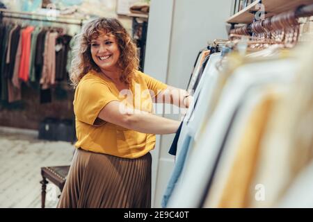 Woman working in a clothing shop. Female owner looking away and smiling while helping a customer to buy in a fashion store. Stock Photo