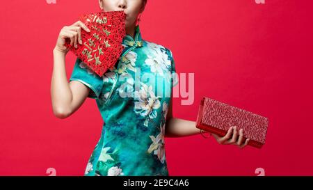 Woman wearing oriental qipao dress holding Ang Pao or red envelopes and wallet in hands on studio background for Chinese new year spending concepts, t Stock Photo