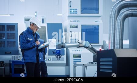Chief Engineer Wearing Safety Vest and Hard Hat, Use Digital Tablet in Modern Factory, Optimizing Production Line. Industrial Facility: Professionals Stock Photo