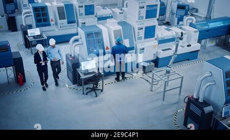 Industry Four Factory: Female Executive and Chief Engineer Inspect Facility Workshop, Look at robot arm working on Assembly Line. High-End CNC Stock Photo
