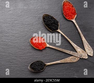 black caviar of paddlefish fish and red chum salmon caviar in a spoon, black background, top view.