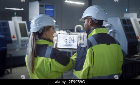 Industry 4.0 Factory: Chief Engineer and Project Supervisor in Safety Vests and Hard Hats, Talk, Use Digital Tablet Computer, Screen Shows 3D Concept Stock Photo