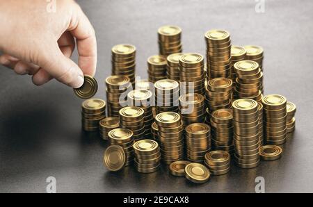 Human hand stacking many golden coins over black background. Concept of income saving and wealth. Composite image between a hand photography and a 3D Stock Photo