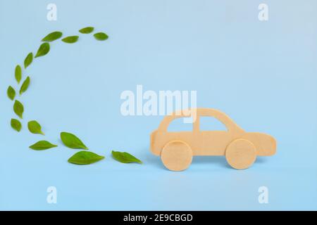 Wooden car model emitting fresh green leaves on blue background. Sustainable, clean and green energy and biofuel and biodiesel for transportation Stock Photo