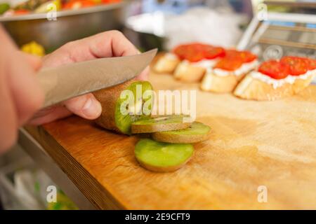 A man cuts a kiwi on a wooden board. Natural light from the window Stock Photo