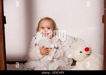 A little girl with toys in a wooden house. Photo studio with Christmas decorations. A happy child plays with toys. Stock Photo