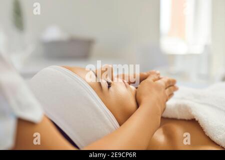 Close up of female beautician hands doing facial massage to attractive girl in bright clinic office. Stock Photo