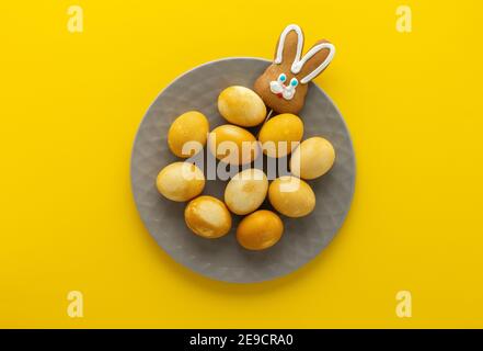 Easter golden painted eggs and biscuits bunny in plate on yellow background, easter festive concept Stock Photo