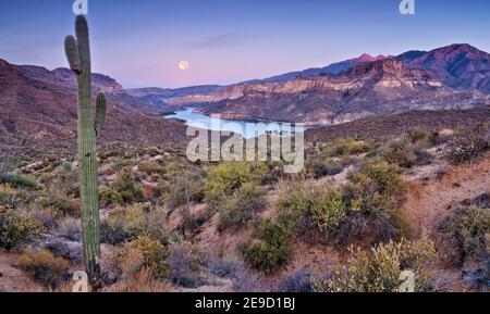 Moon setting down at sunrise over Apache Lake in Superstition Mountains, view from Apache Trail road, Arizona, USA Stock Photo