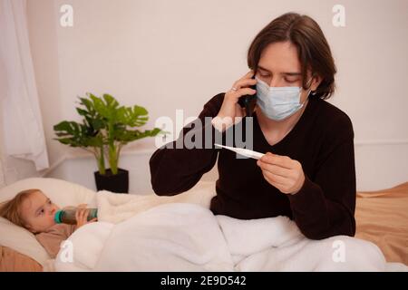 The child is sick, the father in a mask checks the temperature of his daughter. Influenza, cold, coronavirus, covid, home quarantine. The child is sic Stock Photo