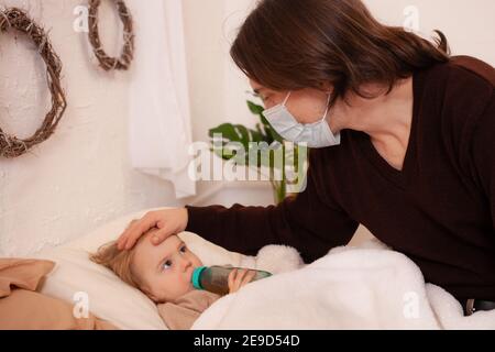 The child is sick, the father in a mask checks the temperature of his daughter. Influenza, cold, coronavirus, covid, home quarantine. The child is sic Stock Photo