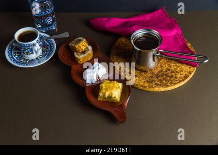 Turkish delight and baclava served with Turkish coffee in cezve with cup, saucer, water glass. Low lighting. Stock Photo