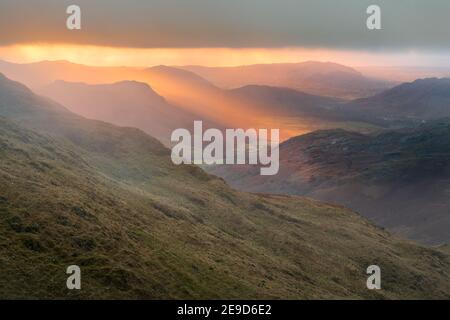 Golden evening light at sunset breaking through clouds onto mountains. Eskdale Valley in the English Lake District. Stock Photo