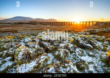 Golden light on a cold Winter evening at Ribblehead Viaduct in North Yorkshire with snow covered rocks in foreground.