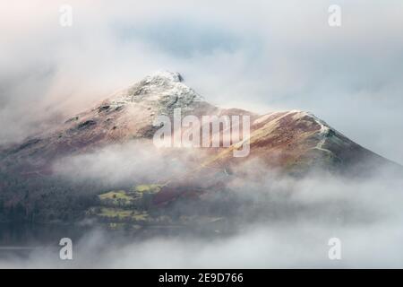 Lake District mountain Catbells covered in low lying misty cloud. Snowcapped moody fell tops. Stock Photo