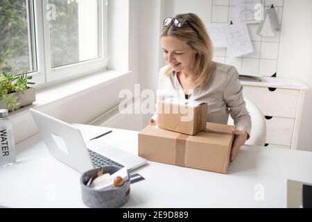 pretty blonde business woman sitting in her office and just got some packages, gifts, delivery from online order and is happy Stock Photo