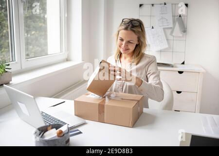 pretty blonde business woman sitting in her office and just got some packages, gifts, delivery from online order and is happy Stock Photo