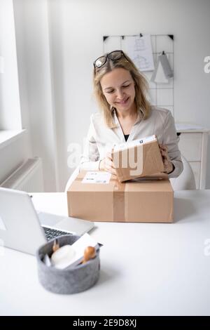 pretty blonde business woman sitting in her office and just got some packages, gifts, delivery from online order and is happy Stock Photo