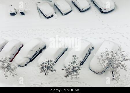 footsteps in the snow next to cars buried by snowfall Stock Photo