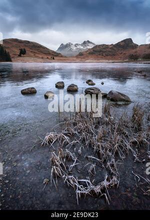 Frozen lake with beautiful view of snowcapped mountains on a Winter morning. Blea Tarn, Lake District, UK. Stock Photo