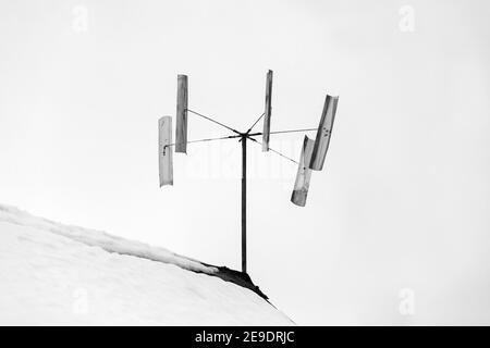 Wind turbine mounted on a rooftop under white sky background. Black and white photo Stock Photo