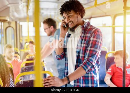 Cute young Afro-American standing in a bus and talking over telephone. Smiling and traveling to his work. Stock Photo