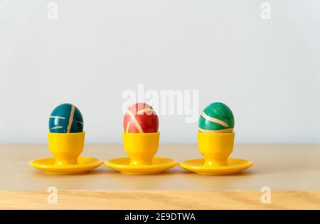 Three colorful painted homemade easter eggs with modern pattern on yellow coasters on wooden table. Easter decoration, easter background  with copy sp Stock Photo