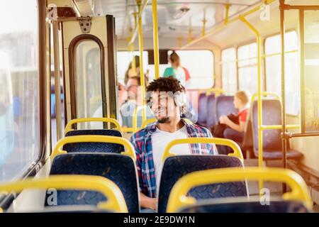 Young modern Afro-American man sitting alone in a public transport and listening to the music. Waiting for bus to move on. Stock Photo