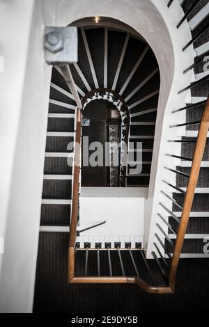 Spiral staircase in old Manor House three floors curving towards floor with wooden banister and old steel heating radiator at the bottom Stock Photo