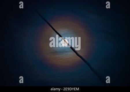 Lunar corona with jet vapour trail crossing in front Stock Photo