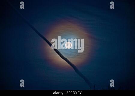 Lunar corona with jet vapour trail crossing in front Stock Photo